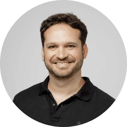 Man with short dark hair and a beard, wearing a black polo shirt, smiling at the camera against a plain light background.