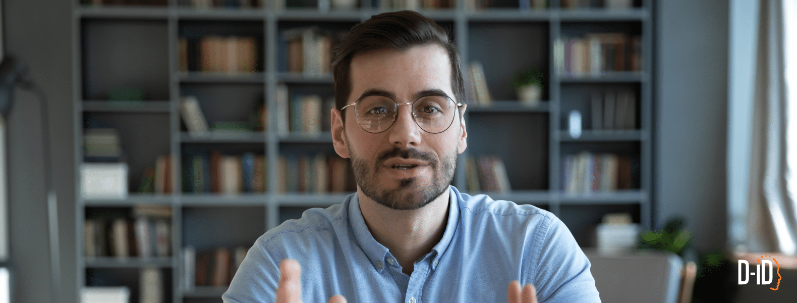 A man with glasses and a beard sits in front of a bookshelf, wearing a light blue shirt, looking directly at the camera—perfect for showcasing explainer videos examples using ai video creation. The D-ID logo is visible in the bottom right corner.
