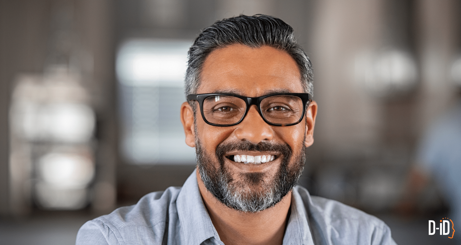 A man with short dark hair, glasses, and a beard smiles at the camera in a softly lit indoor setting, resembling the style of express avatars.