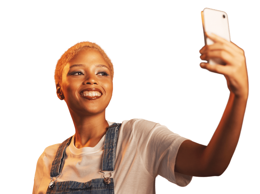 A person wearing a white t-shirt and denim overalls is smiling and holding a smartphone, appearing to take a selfie, reminiscent of the lifelike images created by D-ID Express Avatars.