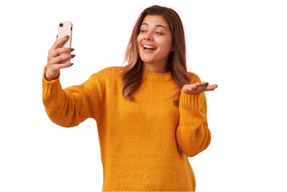 Woman in a yellow sweater smiling and gesturing with her hand while holding a smartphone, appearing to take a selfie or make a video call, perfect for showcasing Premium plus Avatars.