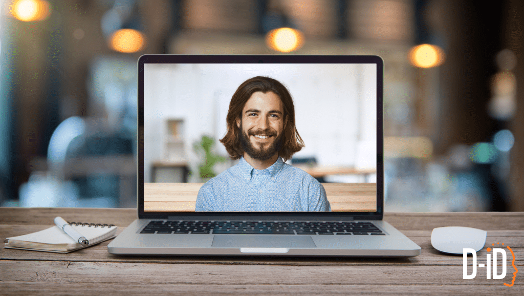 A laptop on a desk displays an ai person video call with a smiling man. A notepad, pen, and wireless mouse are beside the laptop. The D-ID logo is visible in the corner.